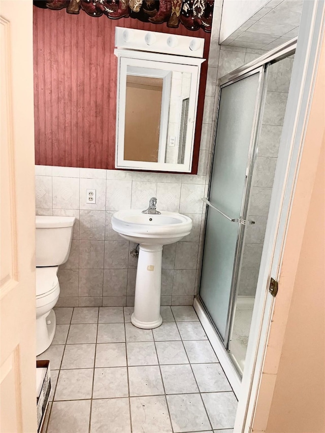 bathroom featuring tile patterned flooring, toilet, a shower with shower door, and tile walls