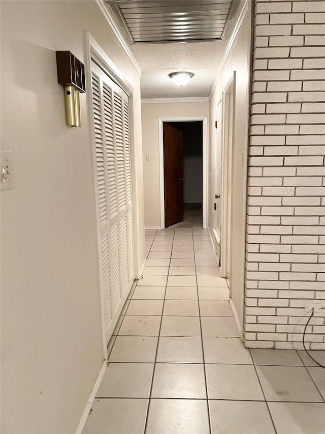 hall with light tile patterned flooring, ornamental molding, and a textured ceiling