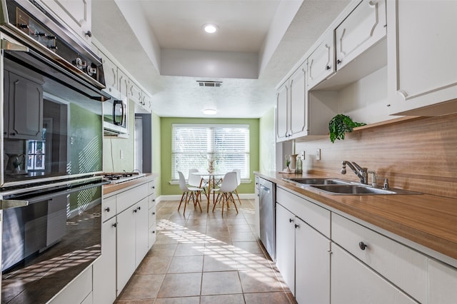 kitchen featuring tasteful backsplash, stainless steel appliances, sink, light tile patterned floors, and white cabinetry