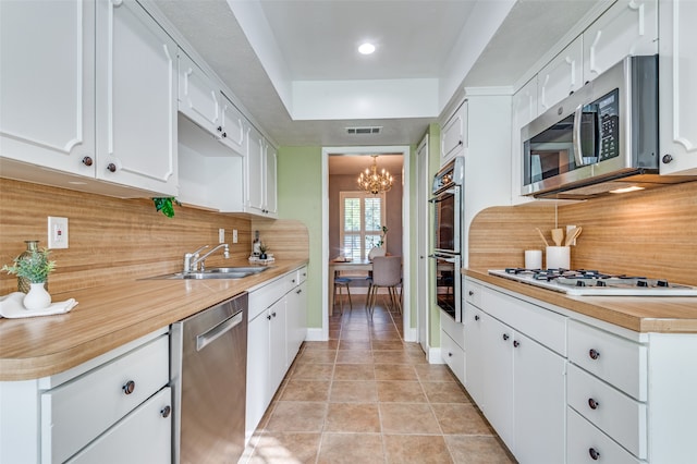 kitchen with white cabinets, decorative backsplash, appliances with stainless steel finishes, and an inviting chandelier