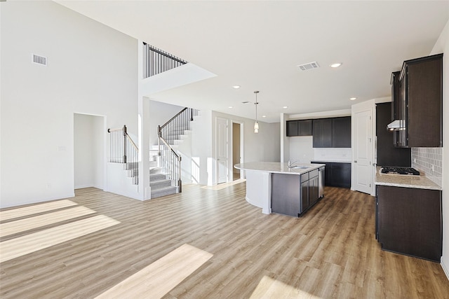 kitchen featuring sink, tasteful backsplash, light hardwood / wood-style flooring, gas cooktop, and a kitchen island with sink