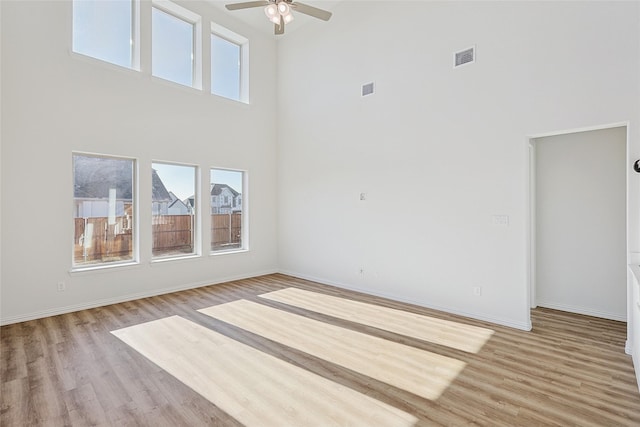 unfurnished living room featuring ceiling fan, a towering ceiling, and light hardwood / wood-style floors