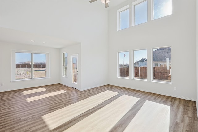 unfurnished living room featuring hardwood / wood-style floors, a towering ceiling, and ceiling fan