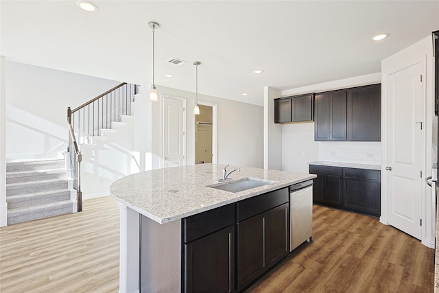 kitchen with dishwasher, wood-type flooring, sink, backsplash, and a center island with sink