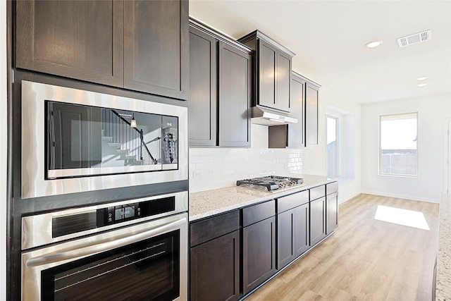 kitchen with dark brown cabinetry, light stone counters, tasteful backsplash, and appliances with stainless steel finishes