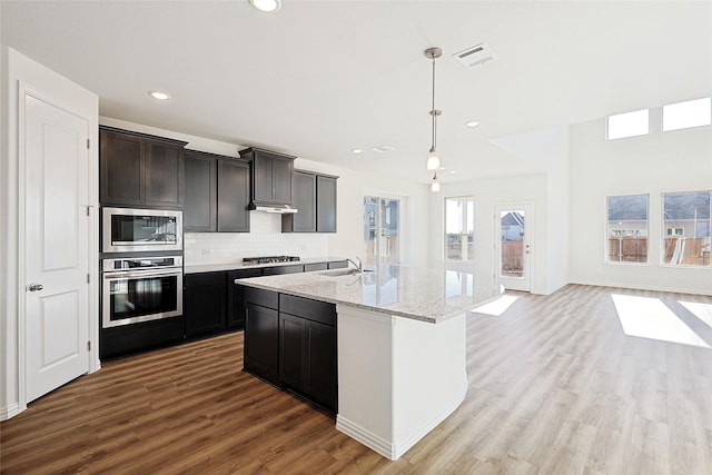 kitchen featuring sink, appliances with stainless steel finishes, pendant lighting, a kitchen island with sink, and backsplash