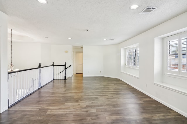 empty room with dark hardwood / wood-style flooring, a textured ceiling, and a chandelier