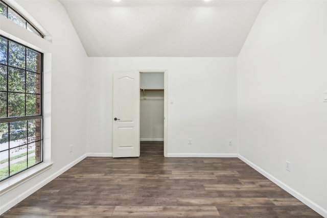 unfurnished bedroom with dark hardwood / wood-style floors, lofted ceiling, a walk in closet, and multiple windows