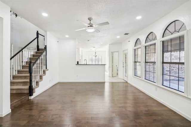 unfurnished living room with ceiling fan with notable chandelier, dark hardwood / wood-style flooring, and a textured ceiling