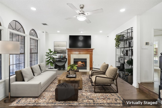 living room featuring ceiling fan, a fireplace, wood-type flooring, and a textured ceiling