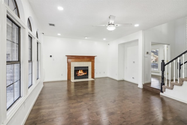 unfurnished living room with a textured ceiling, ceiling fan, a fireplace, and dark wood-type flooring