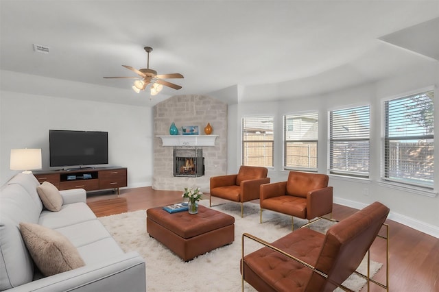 living room featuring lofted ceiling, ceiling fan, hardwood / wood-style flooring, and a stone fireplace