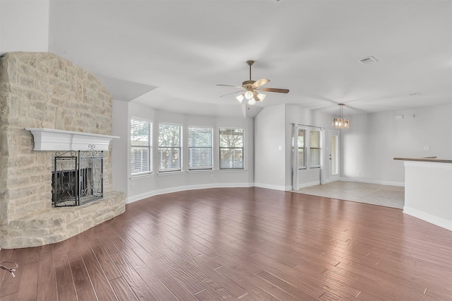 unfurnished living room featuring ceiling fan with notable chandelier, wood-type flooring, and a brick fireplace