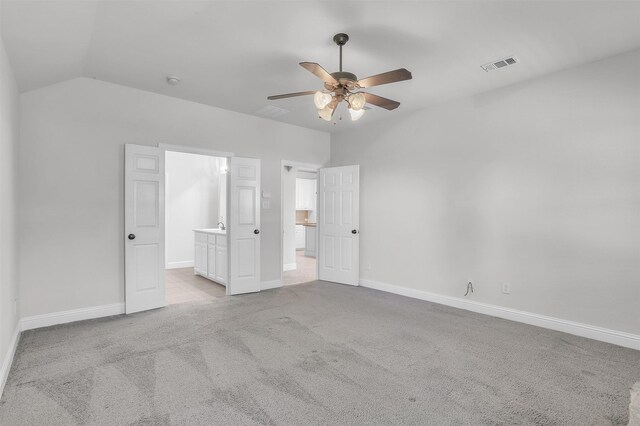 unfurnished bedroom with lofted ceiling, ensuite bath, light colored carpet, and ceiling fan