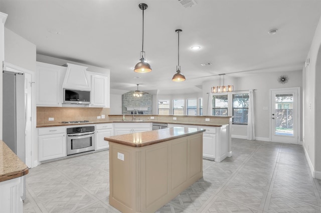 kitchen with appliances with stainless steel finishes, white cabinetry, kitchen peninsula, and a center island