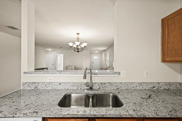 kitchen with kitchen peninsula, light stone counters, sink, pendant lighting, and a chandelier