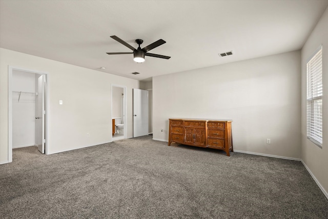 unfurnished bedroom with a walk in closet, ensuite bath, ceiling fan, dark colored carpet, and a closet