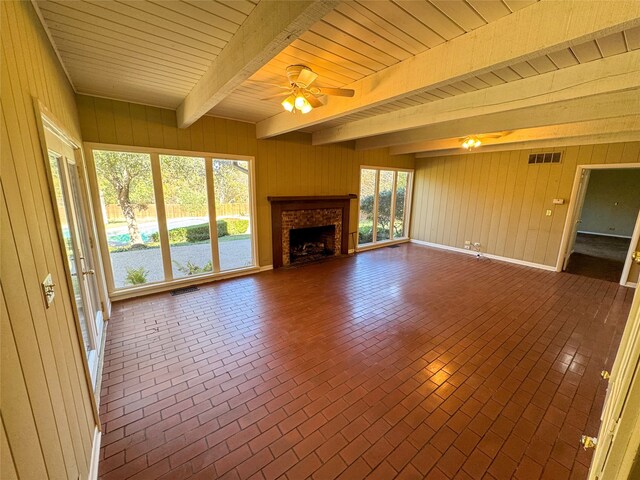 unfurnished living room with beamed ceiling, ceiling fan, wooden ceiling, and wood walls