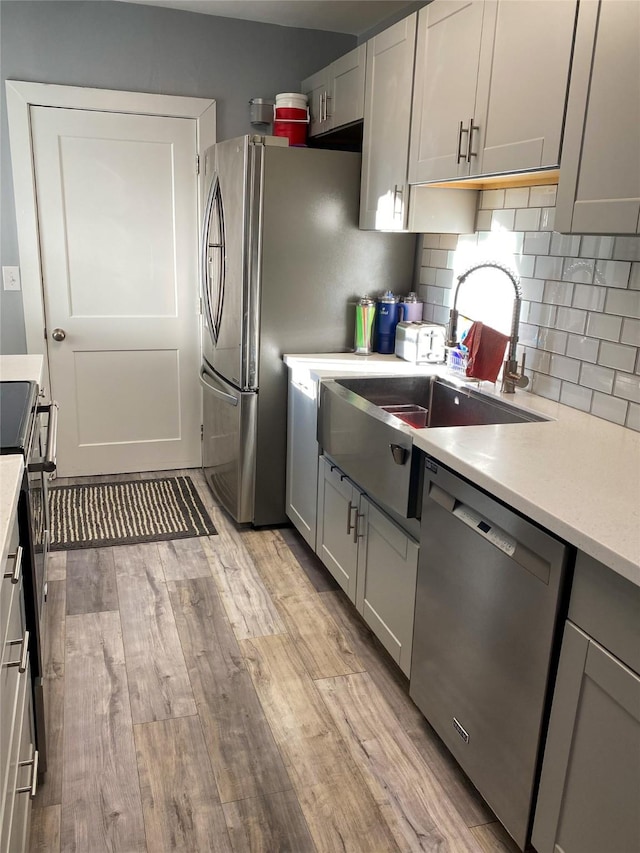 kitchen with gray cabinetry, light hardwood / wood-style flooring, tasteful backsplash, and appliances with stainless steel finishes