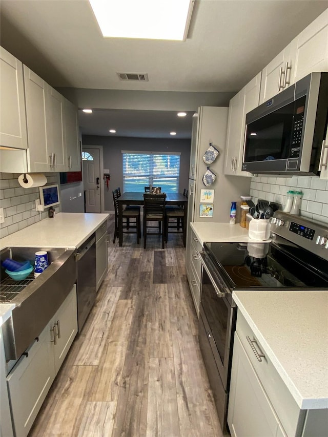 kitchen with stainless steel appliances, hardwood / wood-style floors, white cabinets, and backsplash