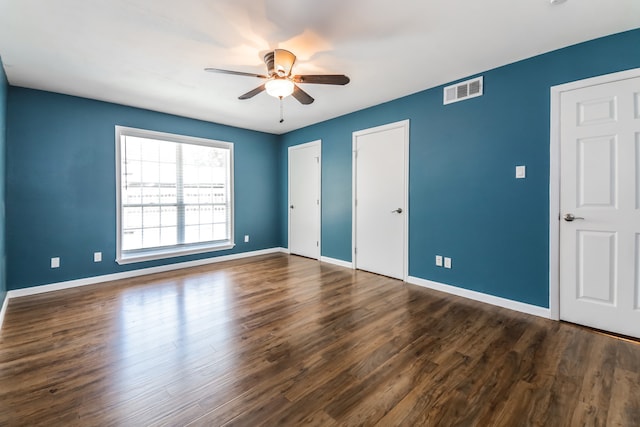 unfurnished bedroom featuring dark hardwood / wood-style floors, ceiling fan, and multiple closets