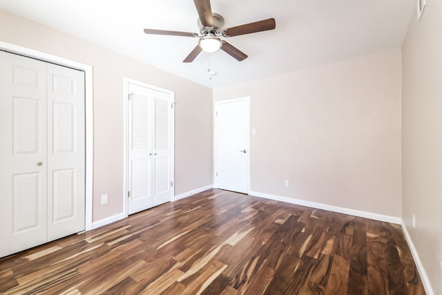 unfurnished bedroom featuring dark hardwood / wood-style flooring, two closets, and ceiling fan