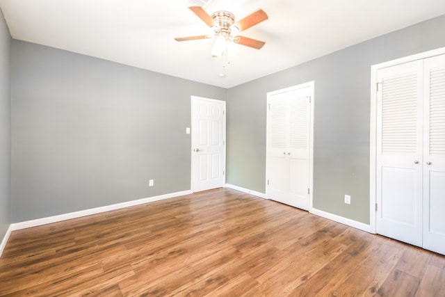 unfurnished bedroom with hardwood / wood-style floors, ceiling fan, and two closets