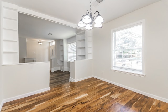 unfurnished dining area featuring a chandelier, dark hardwood / wood-style flooring, and built in features