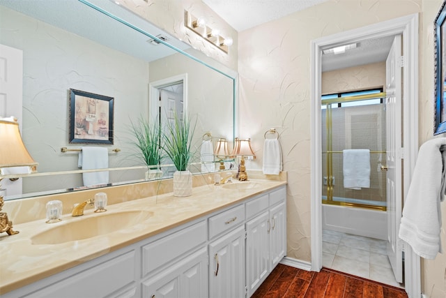 bathroom with hardwood / wood-style floors, vanity, bath / shower combo with glass door, and a textured ceiling