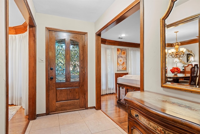 tiled foyer with crown molding and an inviting chandelier