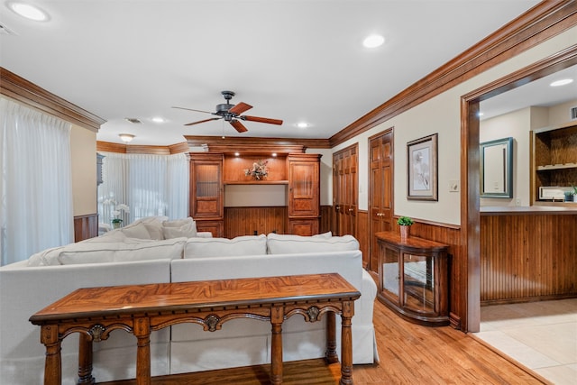 living room featuring ceiling fan, wood walls, ornamental molding, and light hardwood / wood-style flooring