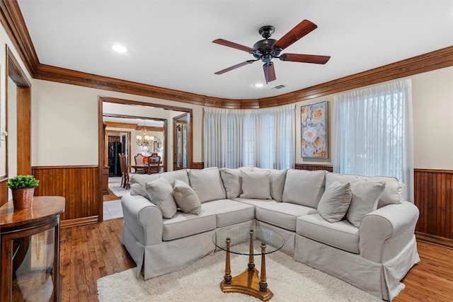 living room featuring hardwood / wood-style floors, ceiling fan with notable chandelier, ornamental molding, and wood walls