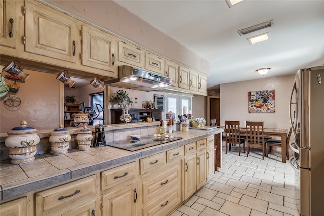 kitchen with stainless steel fridge, black electric cooktop, and tile counters