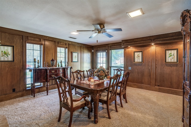 carpeted dining space featuring ceiling fan, wood walls, and a textured ceiling