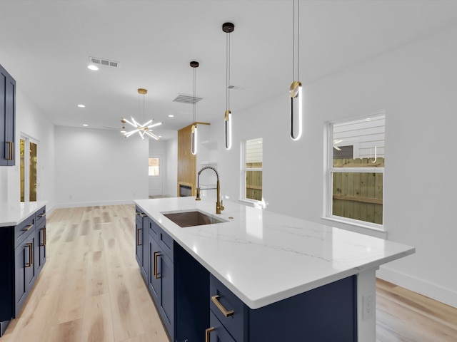 kitchen featuring a center island with sink, blue cabinets, sink, hanging light fixtures, and light wood-type flooring