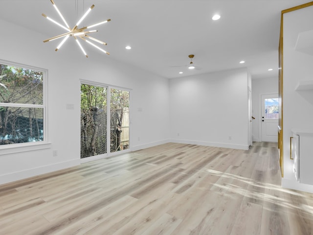 empty room featuring ceiling fan with notable chandelier and light hardwood / wood-style floors