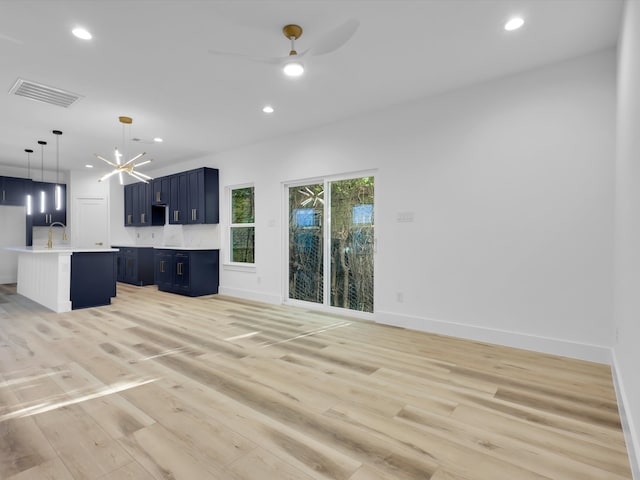 unfurnished living room with ceiling fan with notable chandelier, sink, and light hardwood / wood-style flooring