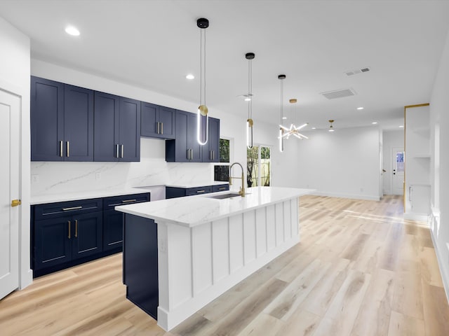 kitchen with backsplash, sink, decorative light fixtures, a center island with sink, and light hardwood / wood-style floors