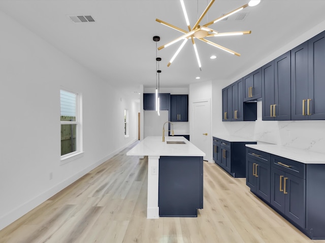 kitchen featuring sink, an island with sink, a chandelier, and light wood-type flooring