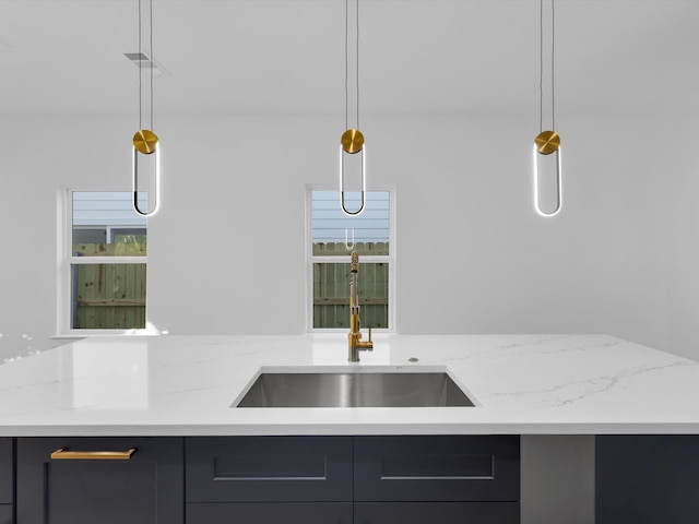 kitchen with plenty of natural light, light stone counters, sink, and decorative light fixtures