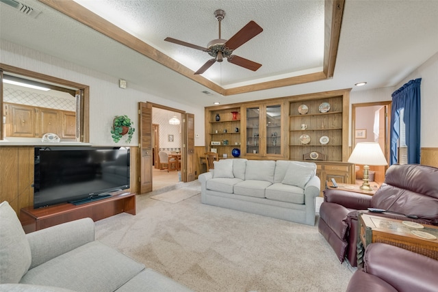 living room with ceiling fan, wood walls, light colored carpet, and a textured ceiling