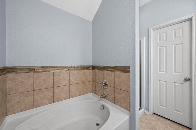 bathroom featuring tile patterned flooring, vaulted ceiling, and a washtub