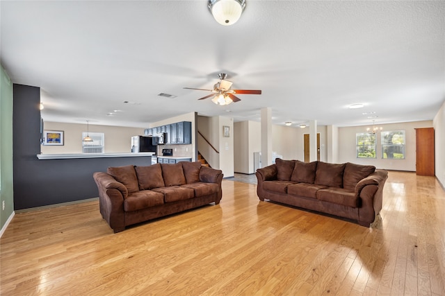 living room with ceiling fan with notable chandelier and light hardwood / wood-style floors