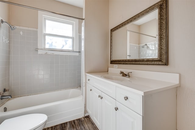 full bathroom with hardwood / wood-style floors, vanity, tiled shower / bath combo, and toilet