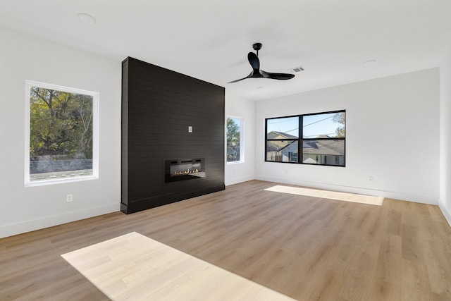 unfurnished living room with a large fireplace, ceiling fan, light hardwood / wood-style flooring, and a healthy amount of sunlight