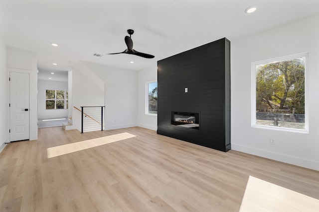 unfurnished living room featuring a fireplace, ceiling fan, plenty of natural light, and light wood-type flooring