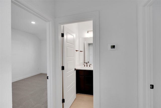 hall with light colored carpet, lofted ceiling, and sink