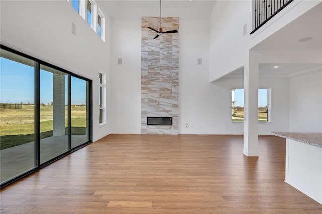 unfurnished living room with a premium fireplace, light hardwood / wood-style flooring, ceiling fan, and a high ceiling