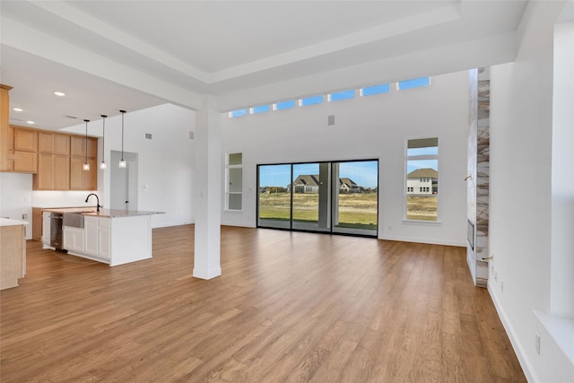 unfurnished living room featuring a towering ceiling, light hardwood / wood-style floors, and sink