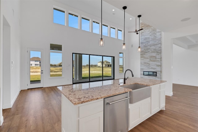 kitchen with white cabinets, sink, stainless steel dishwasher, an island with sink, and decorative light fixtures